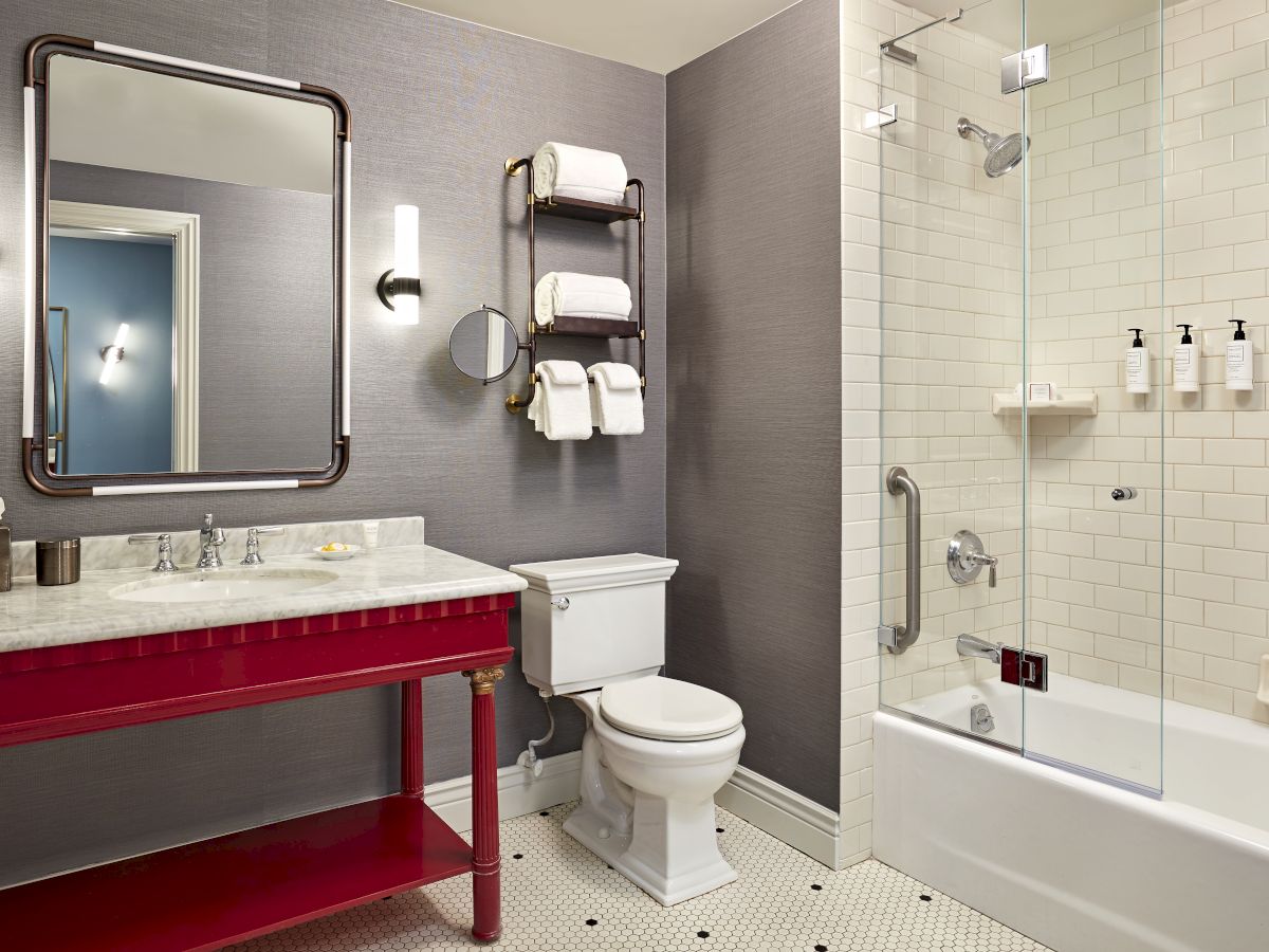Modern bathroom with marble sink, large mirror, towel rack, and glass shower with toiletries.