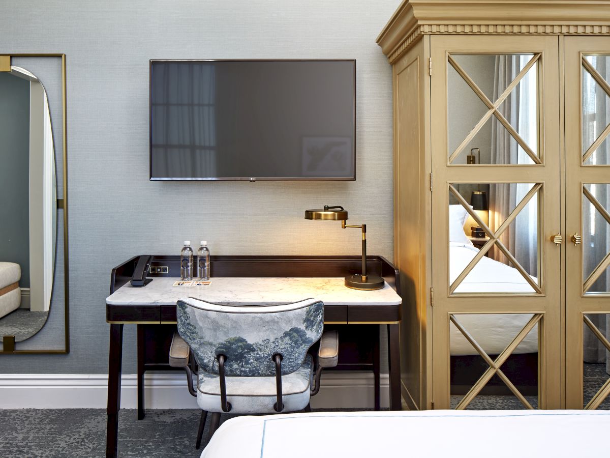 A modern hotel room with a desk, small kettle, TV, mirrors, and wooden doors with diamond glass panels.