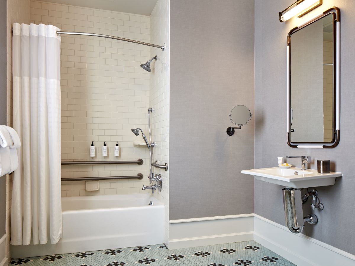 A modern bathroom with a tub, shower fixtures, a small sink, and a backlit mirror.