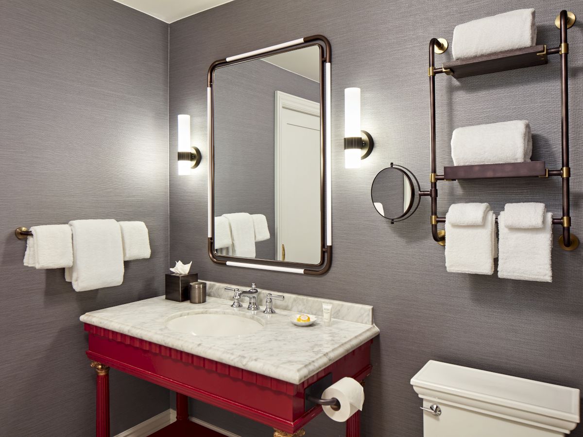 A modern bathroom vanity with a marble sink, mirrors, and neatly stacked white towels on wall racks.