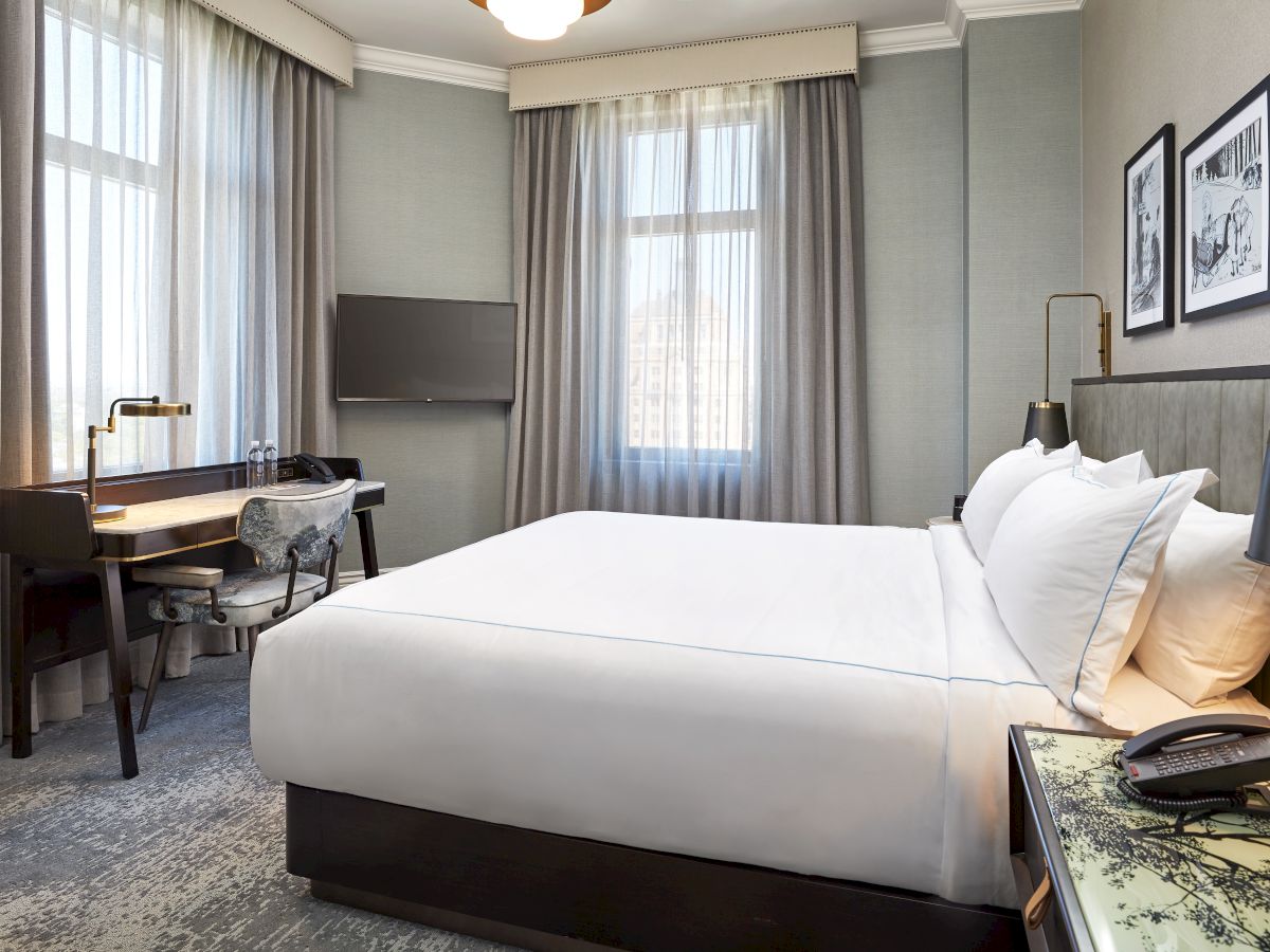 A modern hotel room with a king-size bed, desk, curtains, TV, and wall art by bedside lamps.