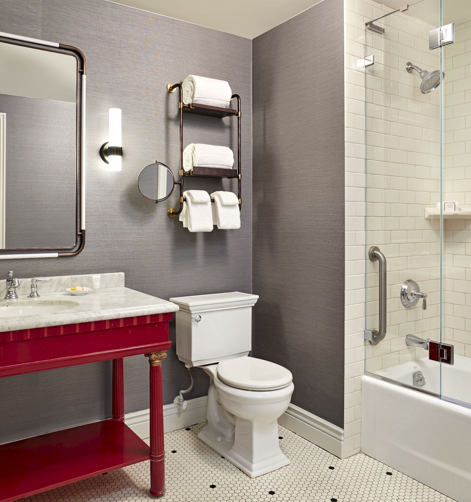 A modern bathroom with a vanity and large mirror, towel rack, and a glass shower/tub with soap bottles.
