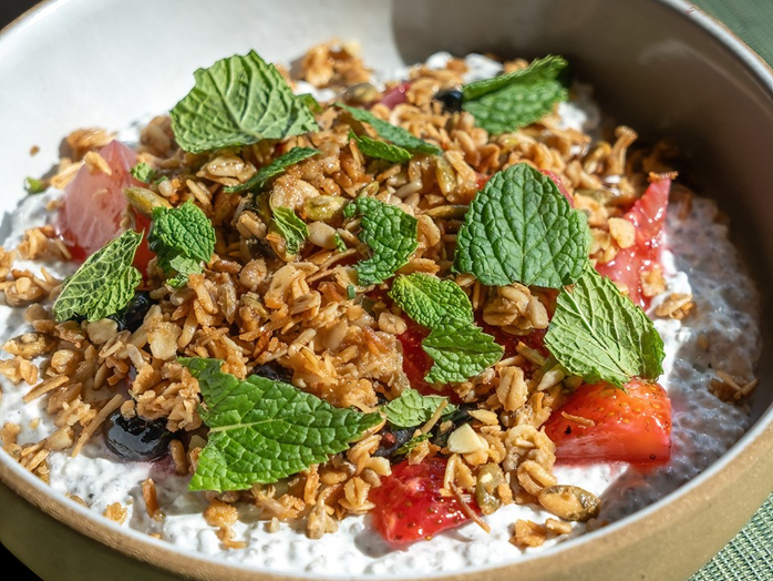 A bowl of yogurt topped with crunchy granola, berries, and fresh mint leaves for a colorful, fresh dessert.