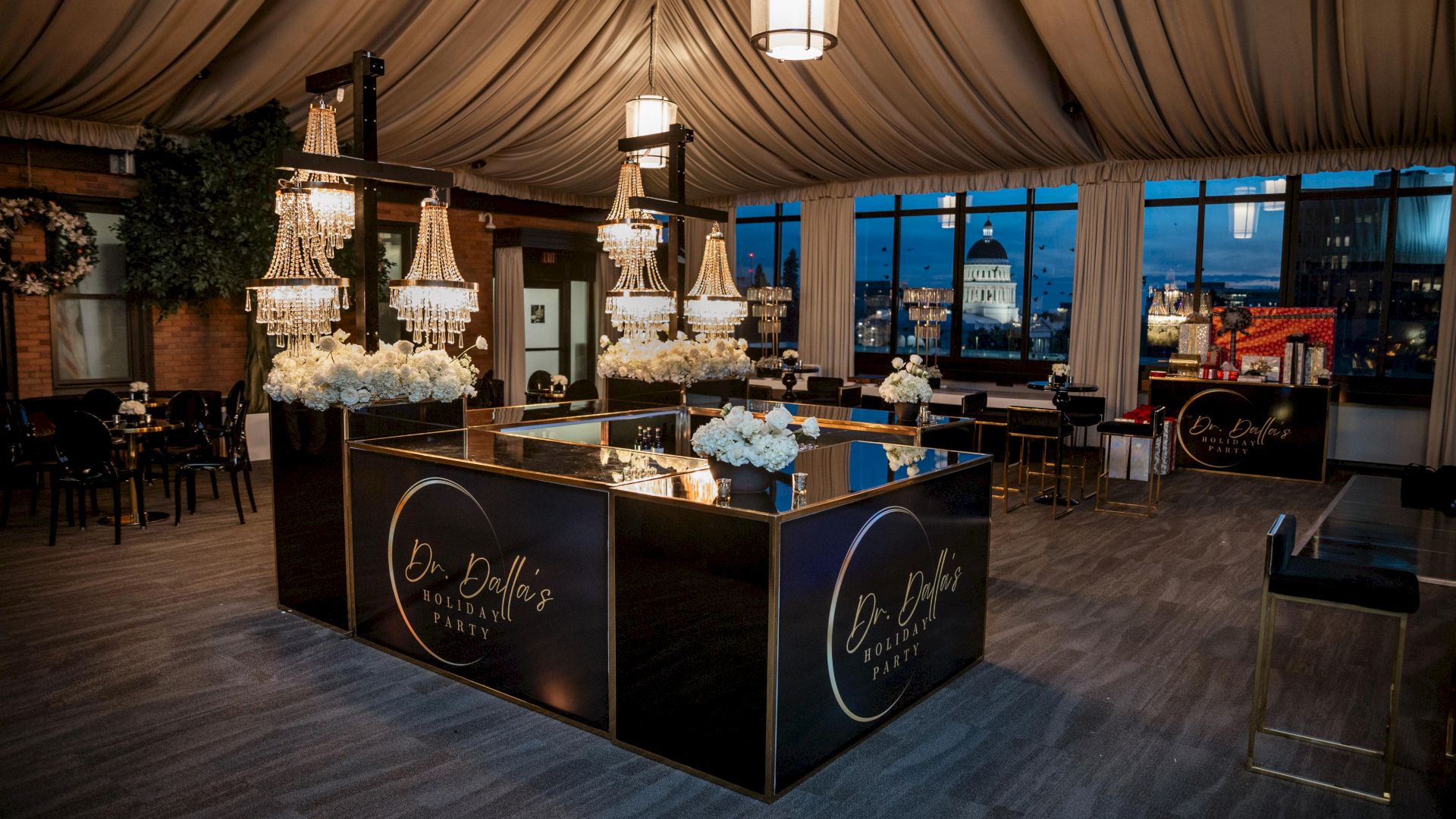 An event bar setup for Dr. Dallas Holiday Party with crystal chandeliers, white flowers, and city views through tall windows.