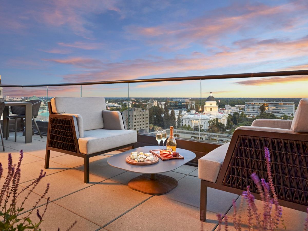 Rooftop terrace lounge with chairs and a table by a sunset city skyline, with the U.S. Capitol building in view.