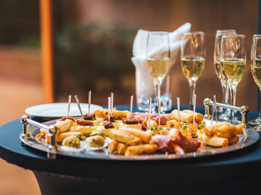 A party platter of assorted bite-size appetizers on skewers with champagne flutes in the background.
