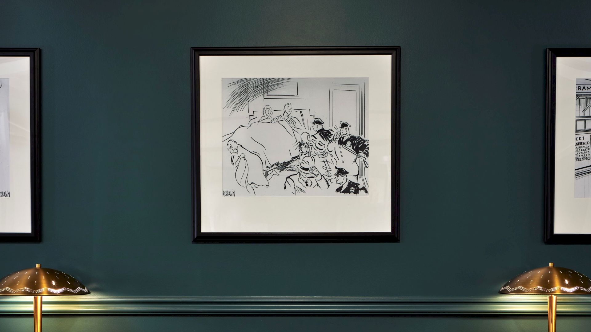 A teal wall displays three framed black-and-white line art illustrations, with two brass dome lamps beneath them and a baseboard trim running along the bottom.