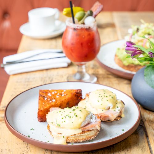 Plate of eggs Benedict with toast, a fresh salad, and a red cocktail topped with fruit and a straw.