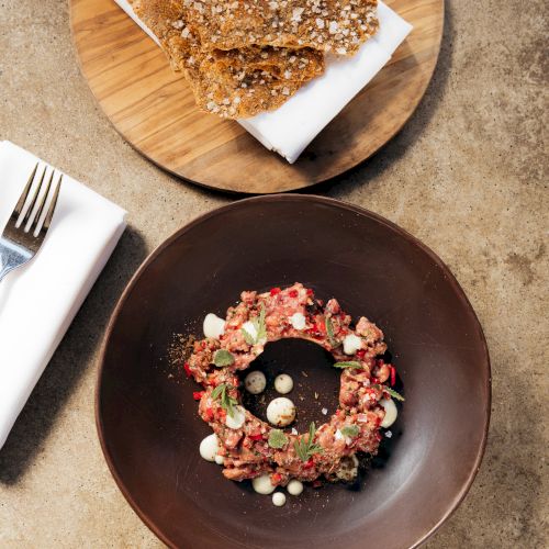 A wooden board of seeded bread and a plate of cured pork with creamy eggs and herbs.