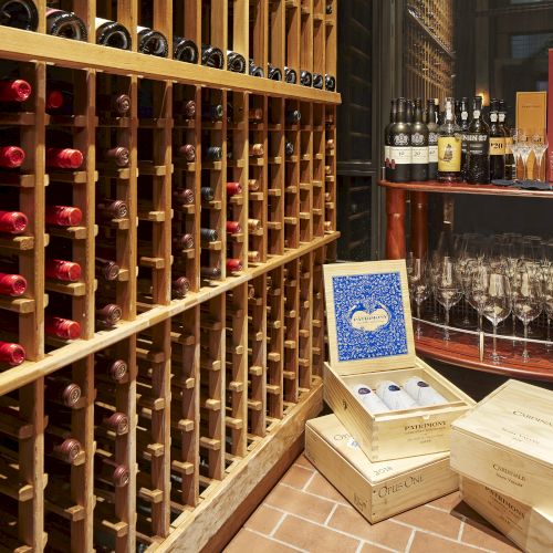 A wine cellar with wooden racks full of bottles, a countertop holding decanters and many glasses, plus boxed wine bottles.