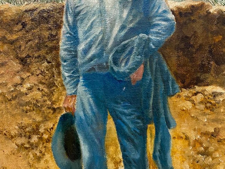 A painted man in a blue tunic stands on a path beside rough earth and stones under a pale sky.