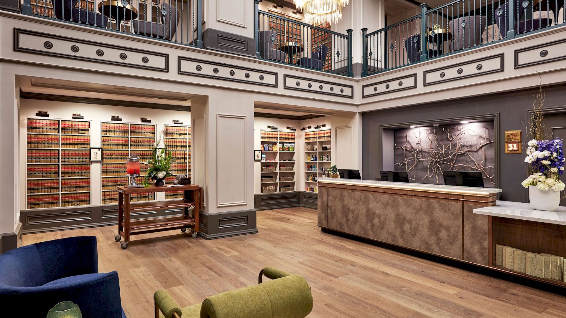 Luxury shop interior with tall shelves, wrought-iron balconies, a bright chandelier, and a reception desk facing decorative wall art.
