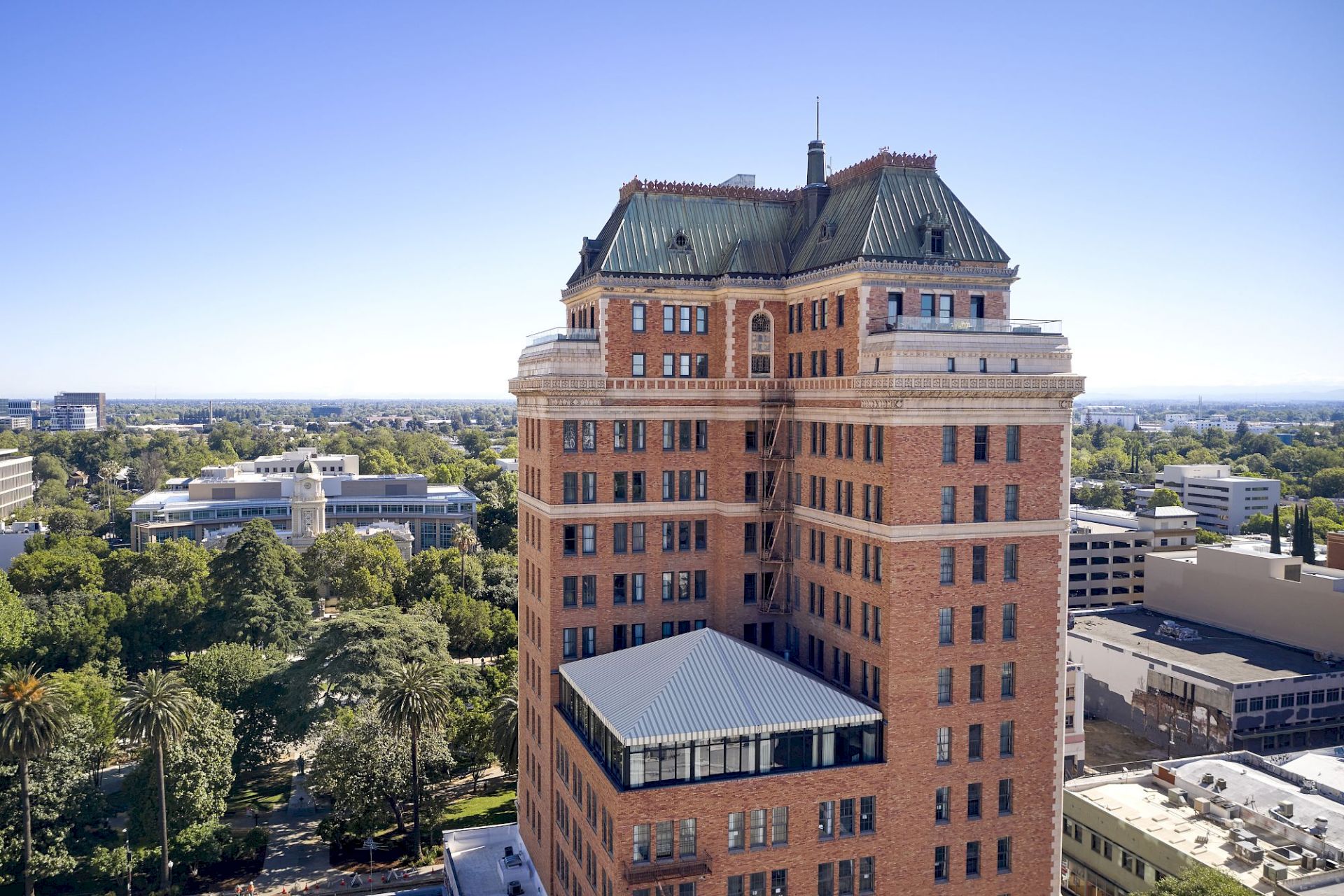 A historic brick campus building with a green metal dome and tall spire rises above trees and surrounding rooftops.