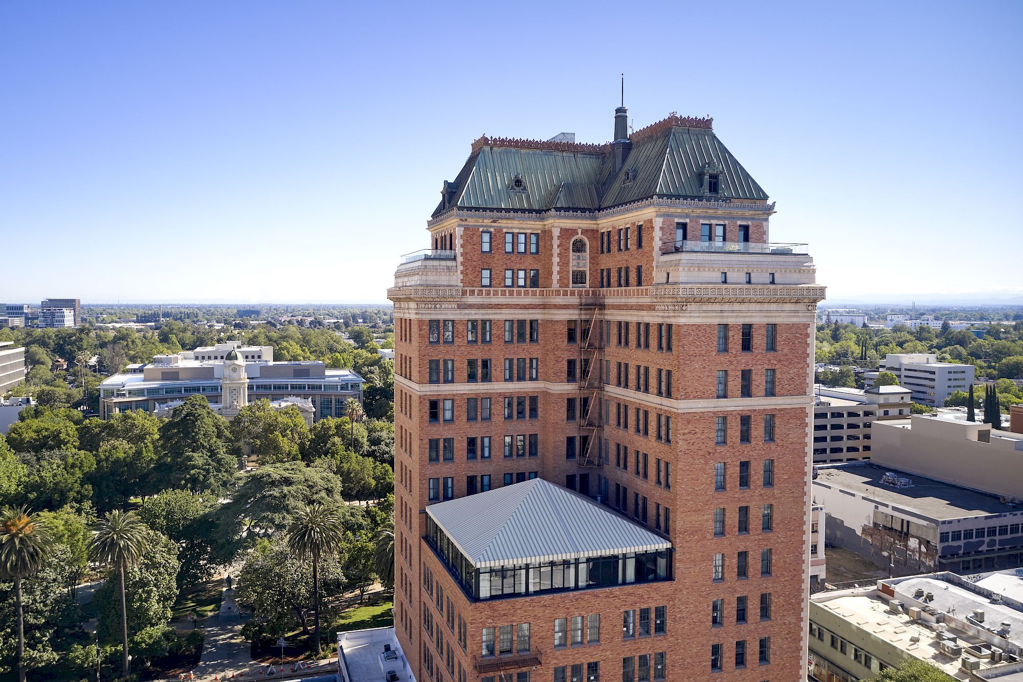 A historic brick campus building with a green metal dome and tall spire rises above trees and surrounding rooftops.